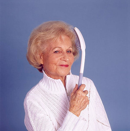 Older woman using a long handle hair brush for easier hair grooming and extra reach