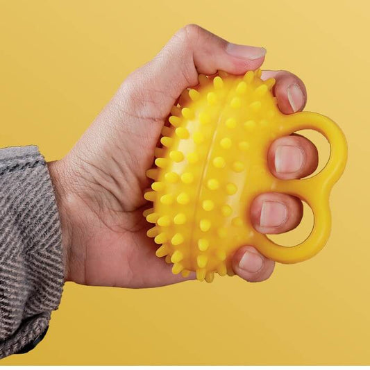 A person's hand using a yellow hand grip exerciser ball, which is a dome-shaped ball with finger slots, soft resistance for stroke and arthritis rehabilitation NZ